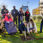 people stood at a park next to a dug up hole, burying a capsule into it