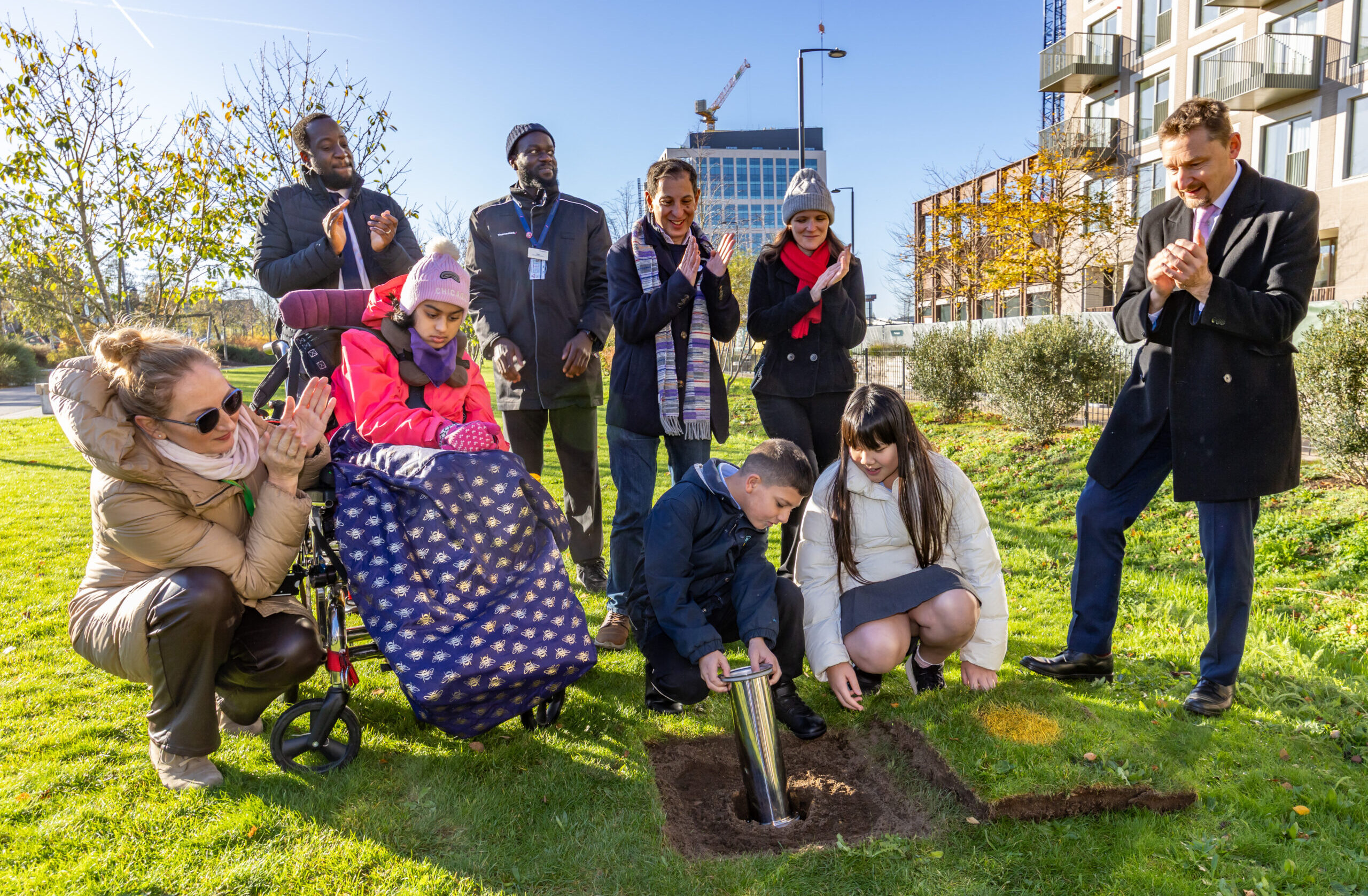 people stood at a park next to a dug up hole, burying a capsule into it
